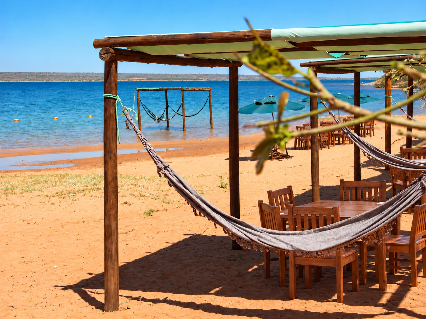 Rede na praia do Village, com mesas e cadeiras de madeira e vista para o Lago de Itaparica